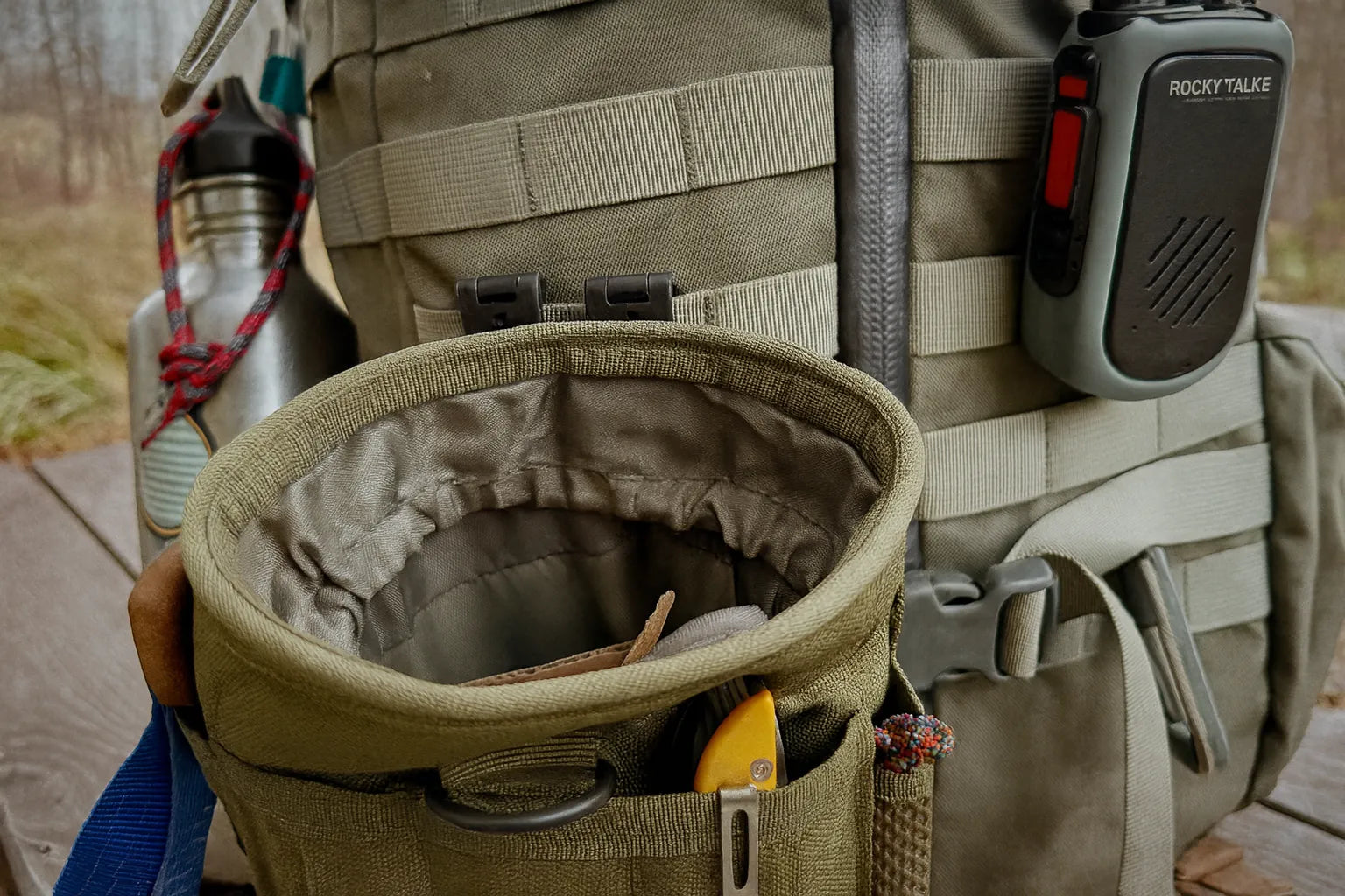 Poche tactique modulaire accrochée à un sac bushcraft avec accessoires visibles.