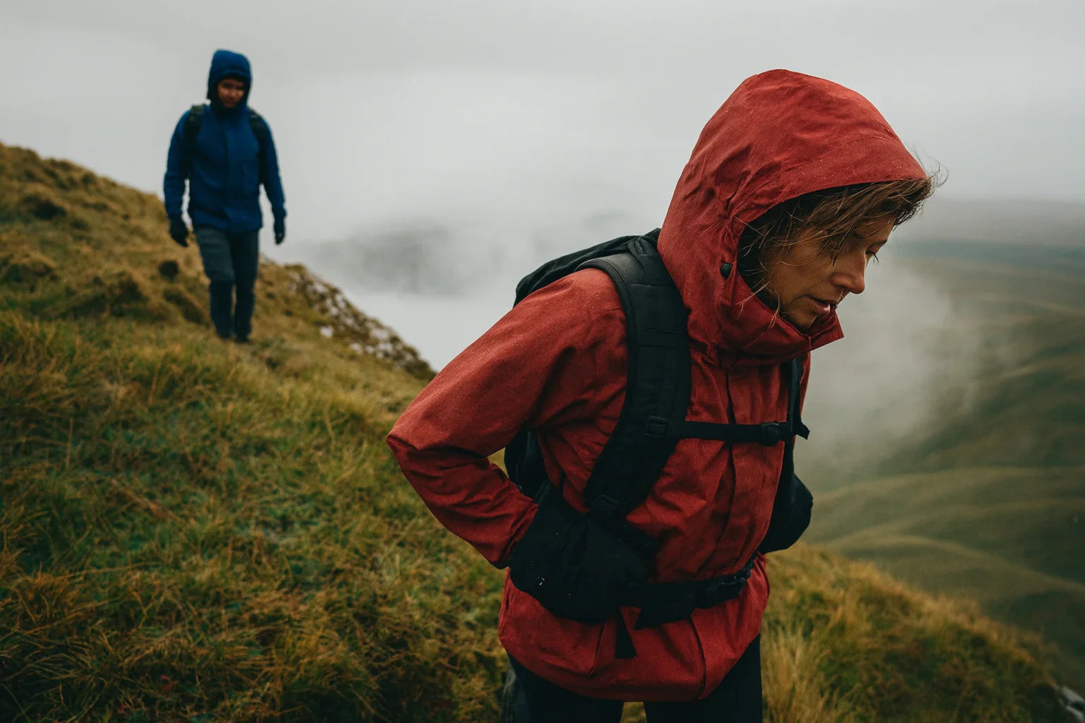 Randonneuse en veste imperméable rouge marchant sous la pluie en montagne.