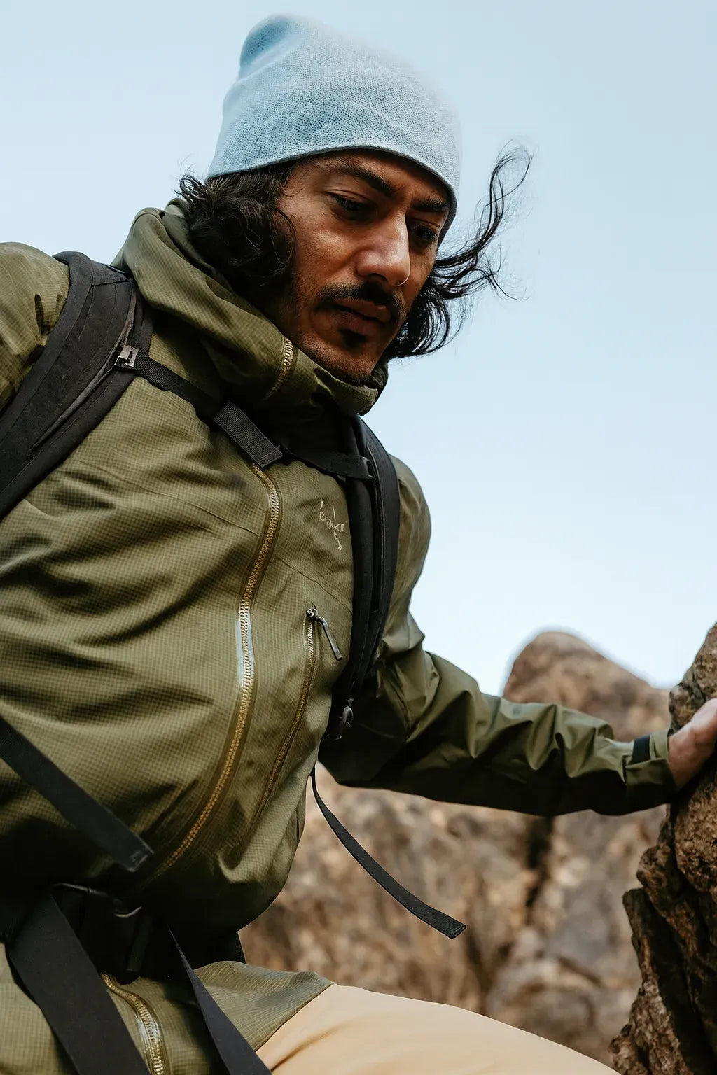 Homme en veste verte escaladant des rochers en montagne.