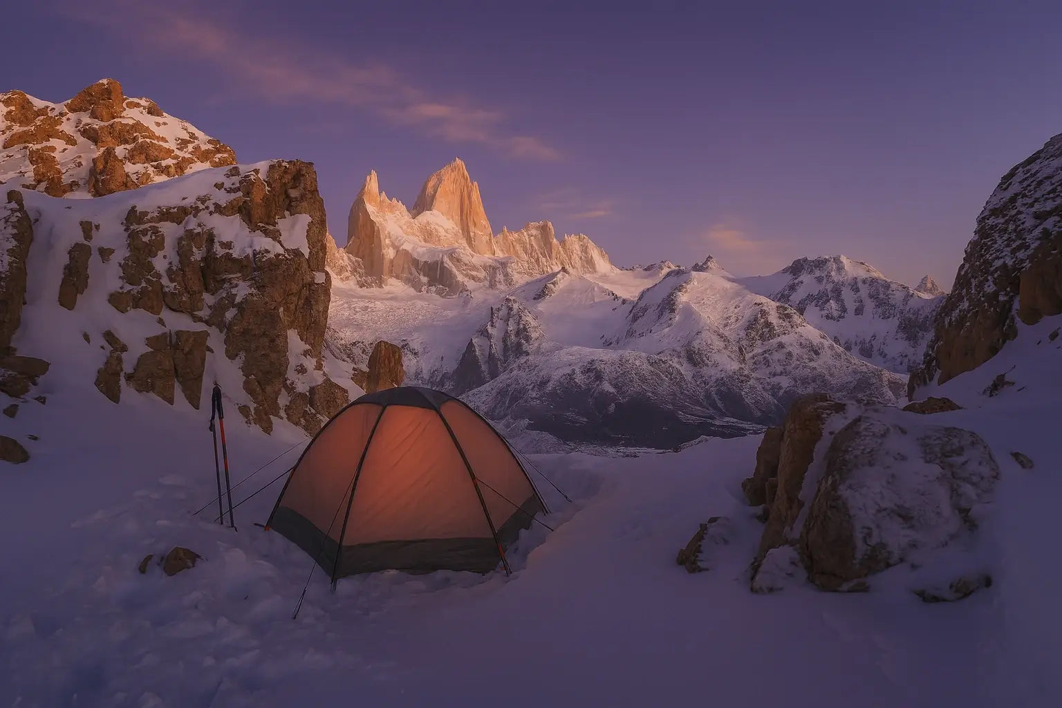 Bivouac hivernal en Patagonie avec tente orange éclairée au crépuscule, installée dans un cirque enneigé face au massif du Fitz Roy baigné par les dernières lueurs du jour.