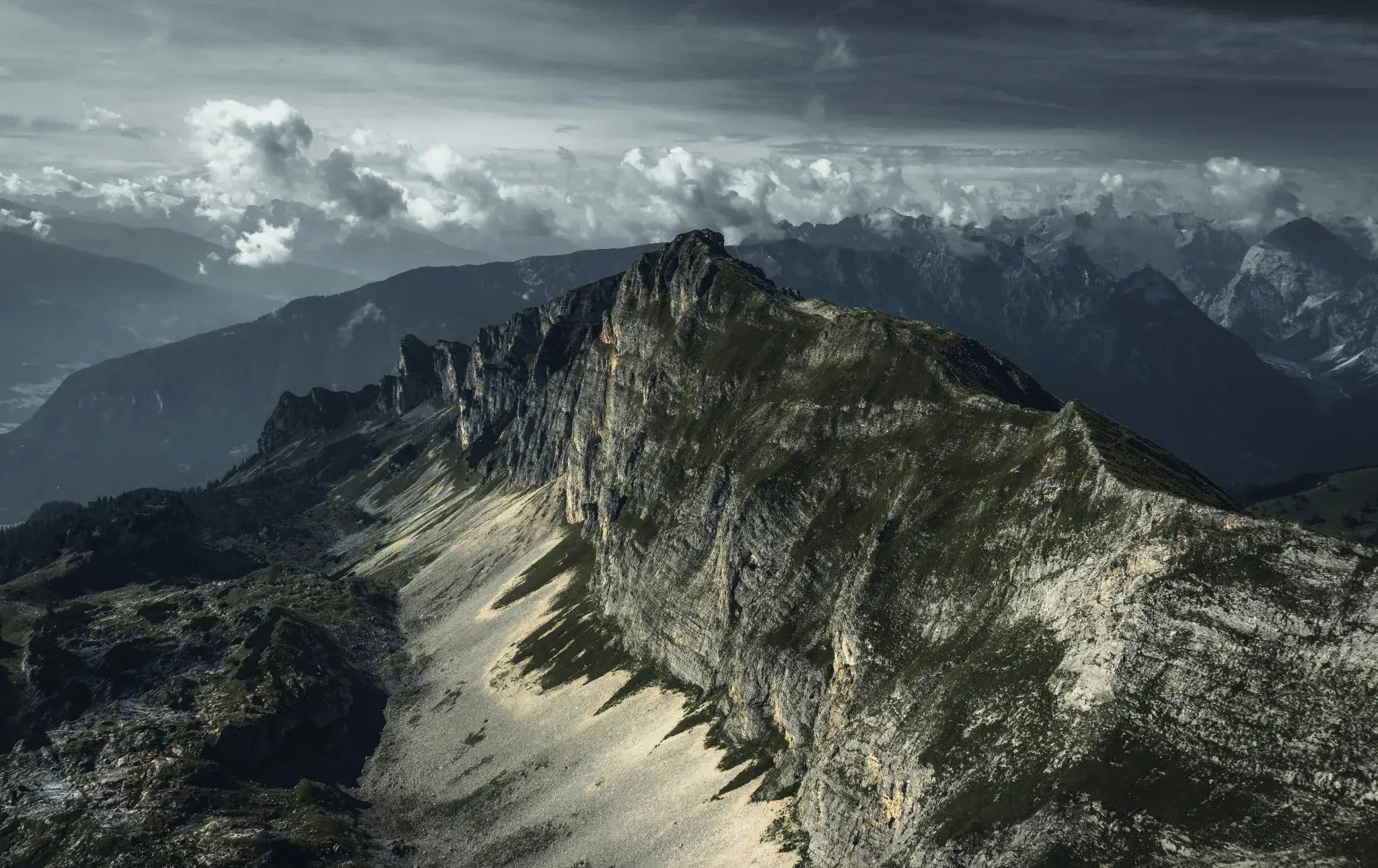 Crêtes rocheuses escarpées vues du ciel avec panorama alpin et ciel nuageux.