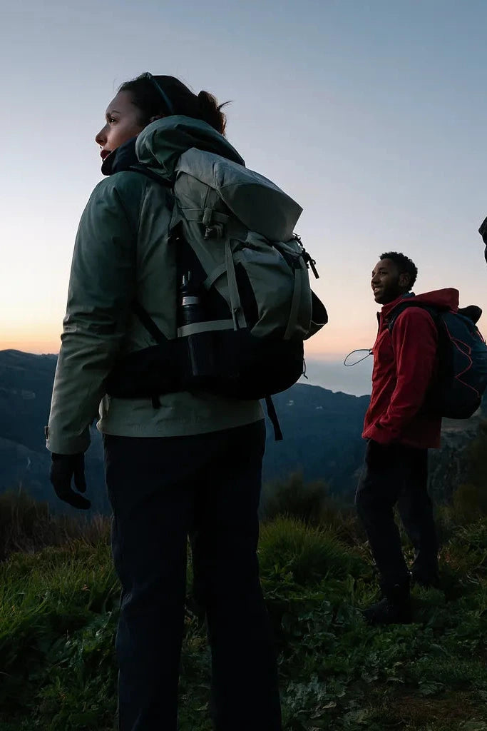Trois randonneurs equipes de sacs a dos et materiel de bivouac observent le paysage montagneux au crepuscule mobile.