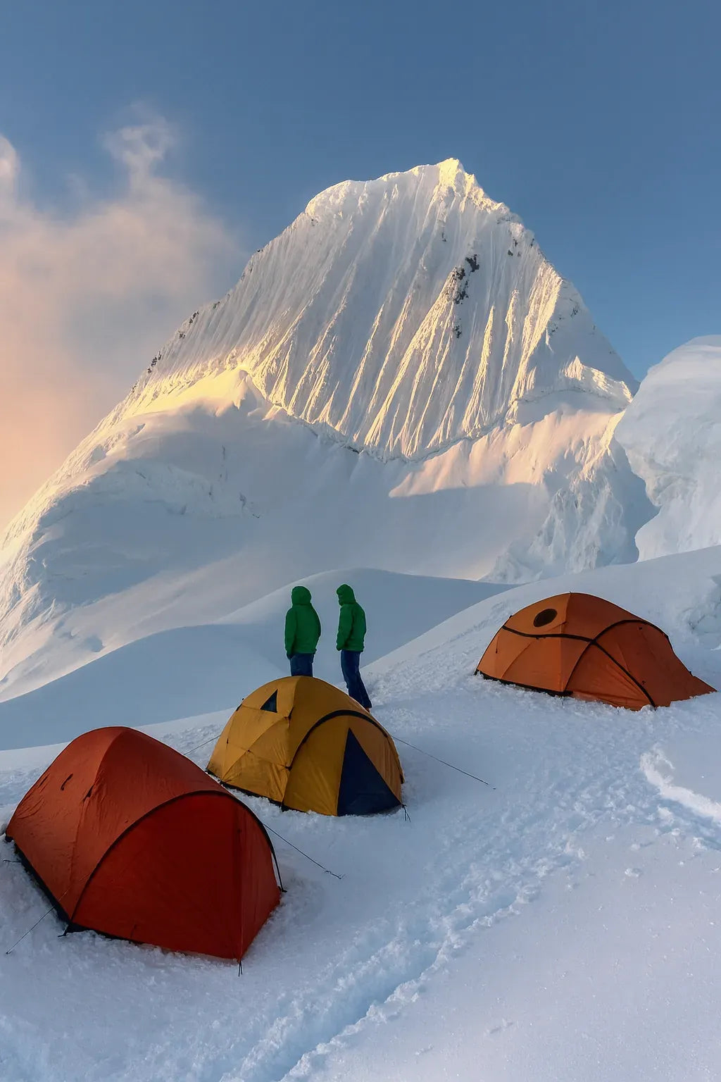 Tentes colorées installées sur la neige face à un sommet enneigé.