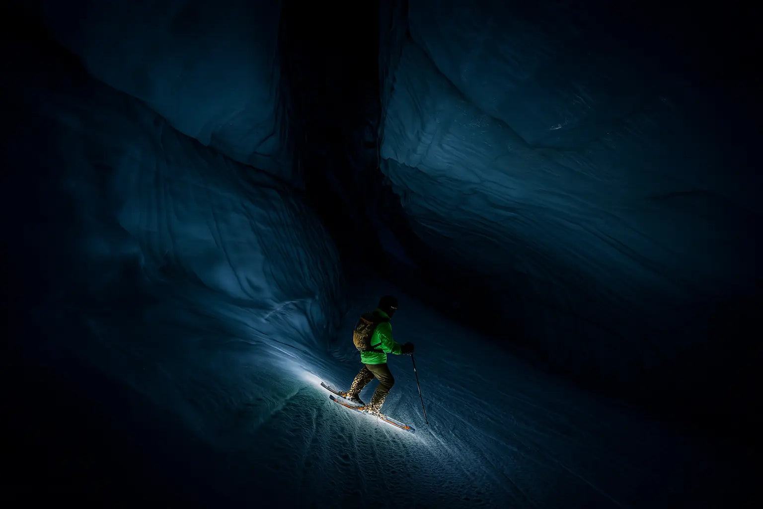 Skieur de randonnée explorant une grotte glaciaire illuminée de nuit.